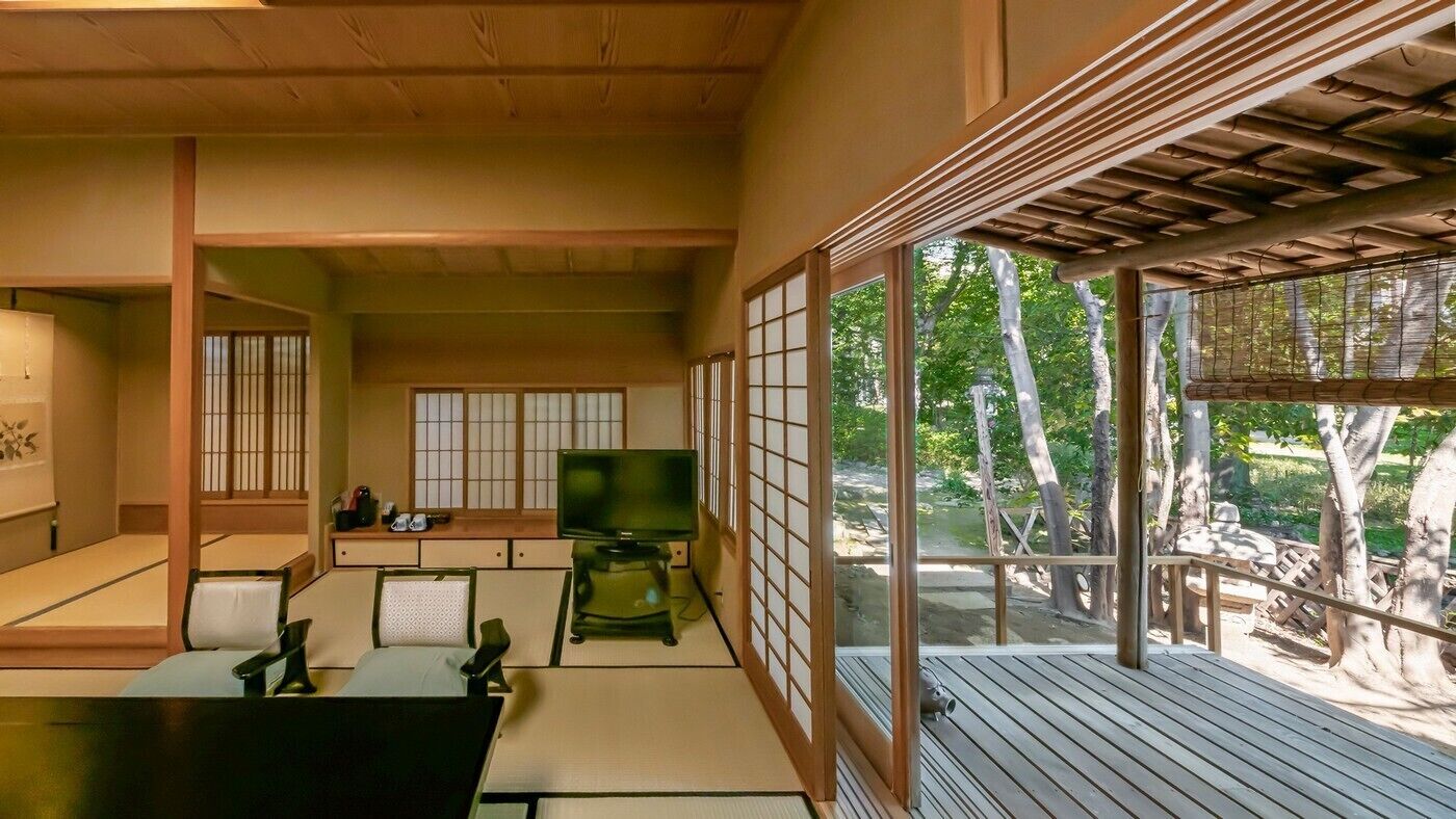 A traditional Japanese room with tatami flooring, a television, and a view of a garden.