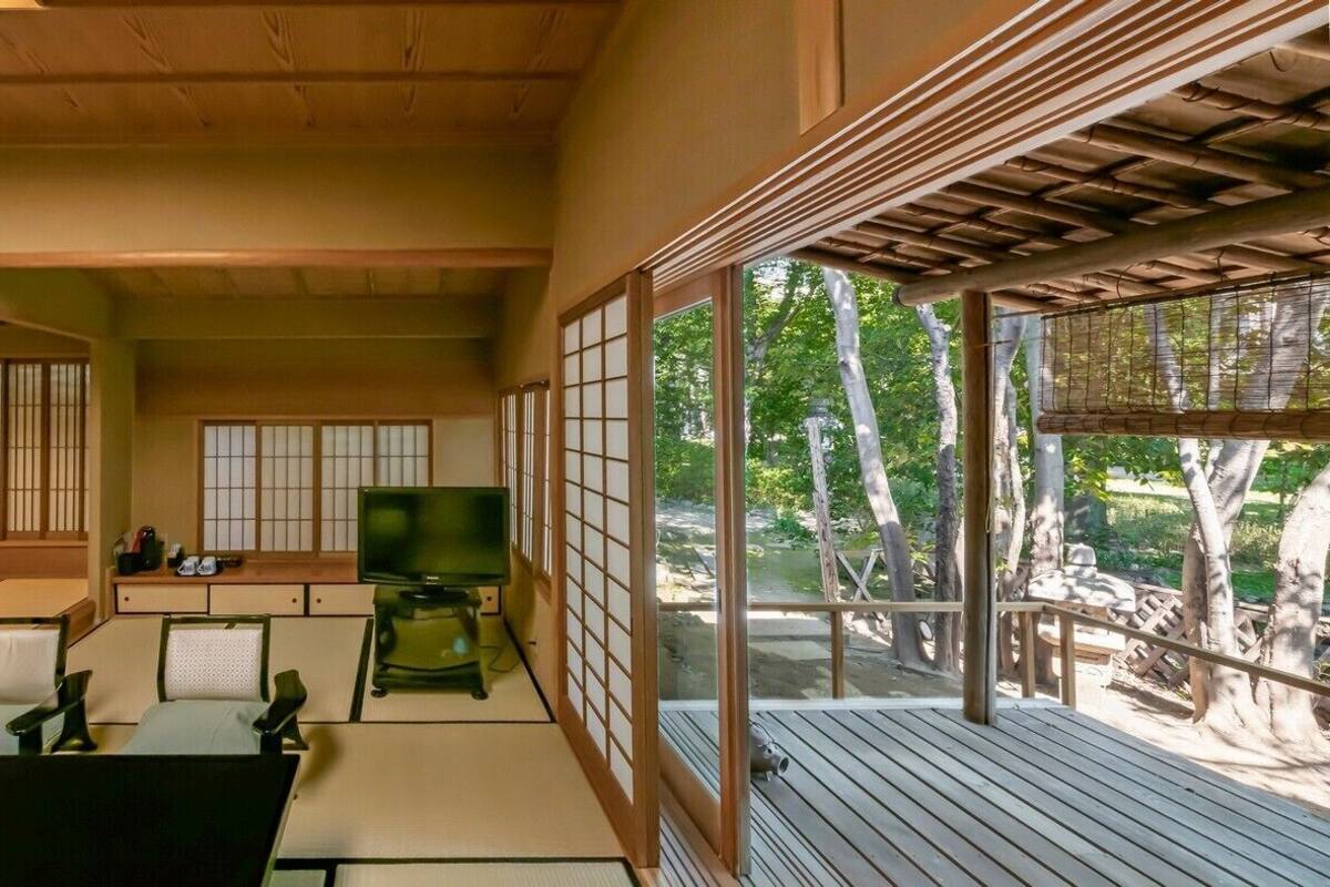 A traditional Japanese room with tatami flooring, a television, and a view of a garden.