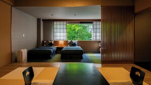 A hotel room with two beds, a desk with chairs, a large window with a view of greenery, and a sliding door. - Tokiwa Hotel (Kofu)