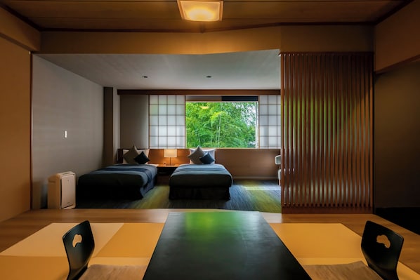 A hotel room with two beds, a desk with chairs, a large window with a view of greenery, and a sliding door. - Tokiwa Hotel (Kofu)