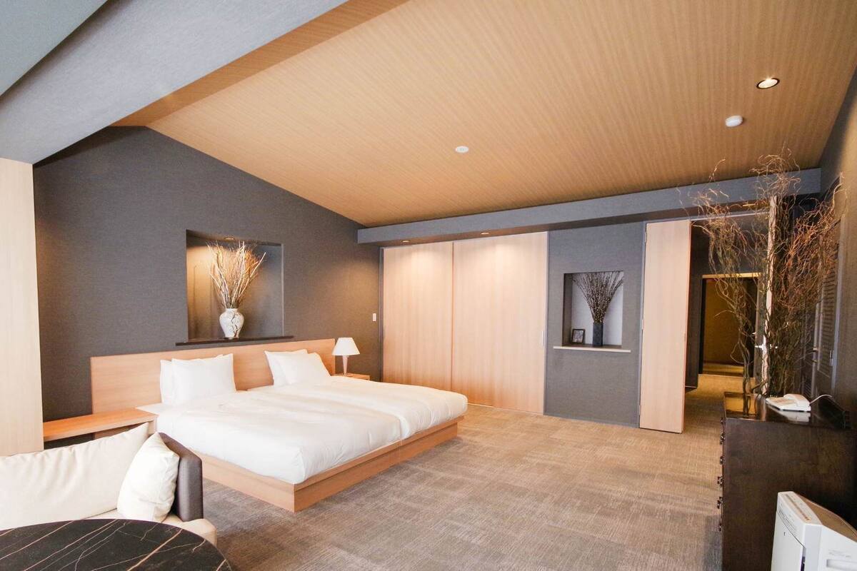 A modern hotel room with a large bed, a desk, and a seating area.