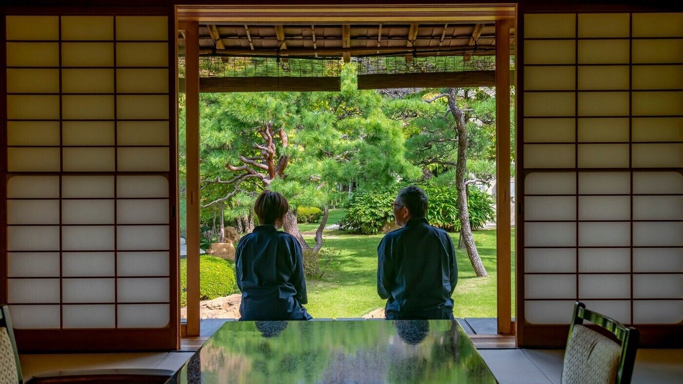 A traditional Japanese room with tatami flooring, a low table, and a view of a garden through a shoji screen.