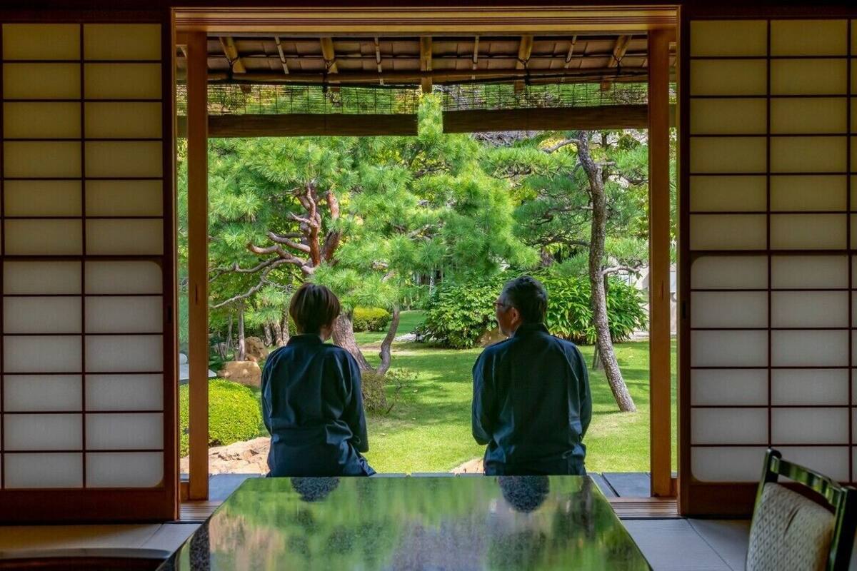 A traditional Japanese room with tatami flooring, a low table, and a view of a garden through a shoji screen.