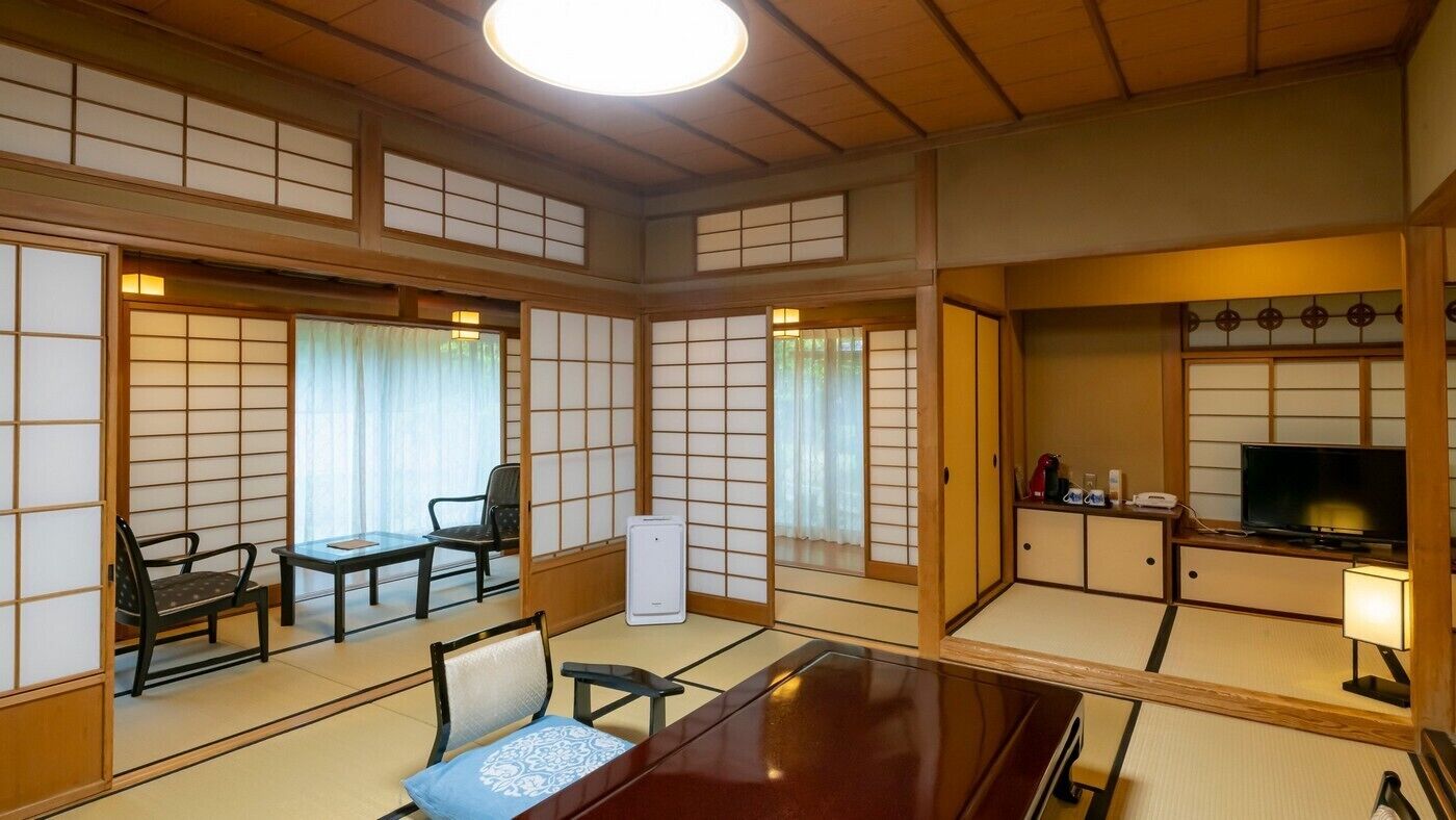 A traditional Japanese room with tatami flooring, a low table, chairs, a television, and a cabinet with a lamp.