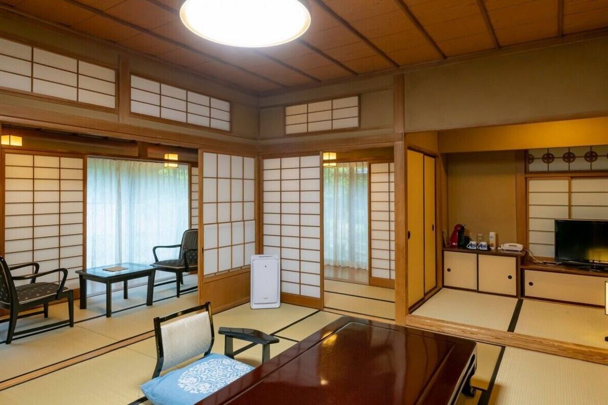 A traditional Japanese room with tatami flooring, a low table, chairs, a television, and a cabinet with a lamp.
