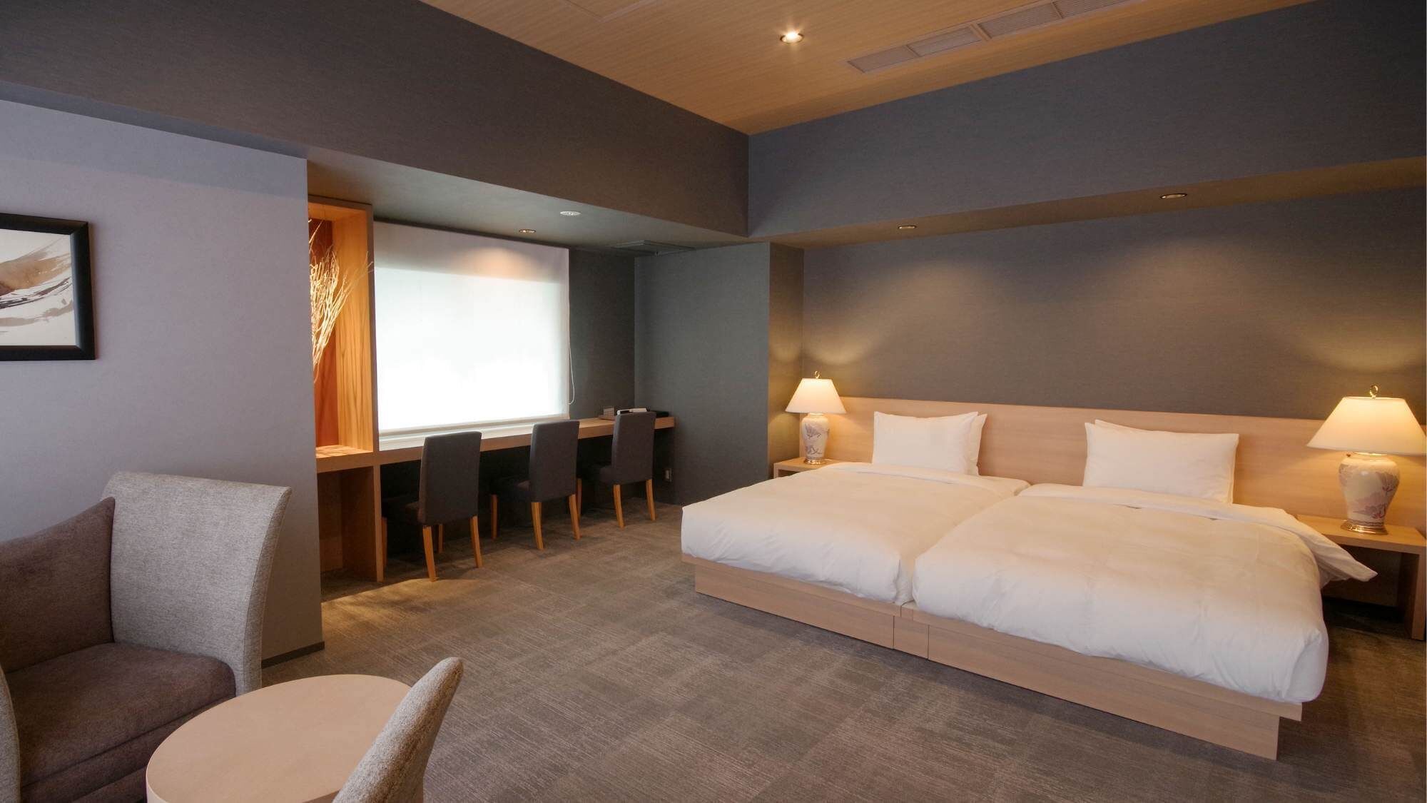 A hotel room with a large bed, a desk with chairs, a small round table, and a sofa.