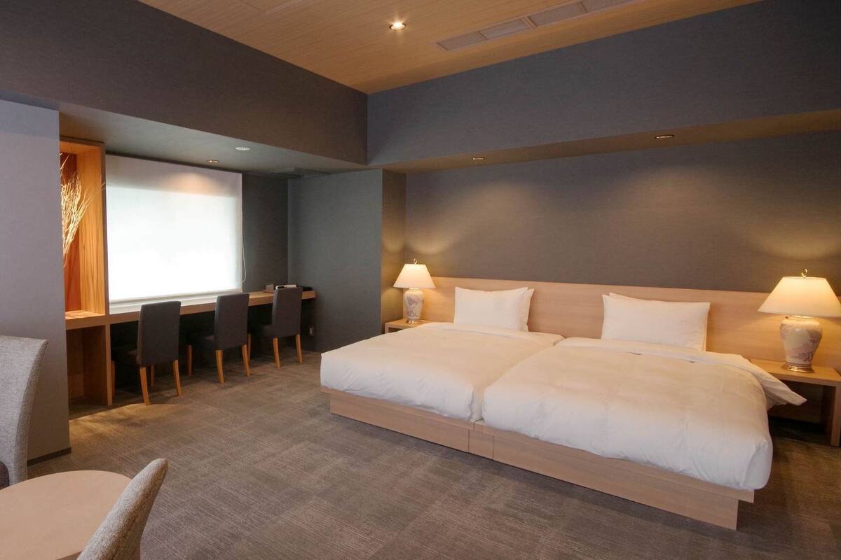 A hotel room with a large bed, a desk with chairs, a small round table, and a sofa.