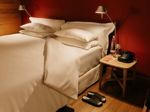 A neatly made bed with white linens, a bedside table with a lamp, a telephone, and slippers on the floor. - Casa Camper Berlin (Berlin)