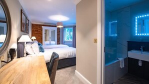 Una habitación de hotel con cama, mesita de noche, lámpara y vistas a un balcón.