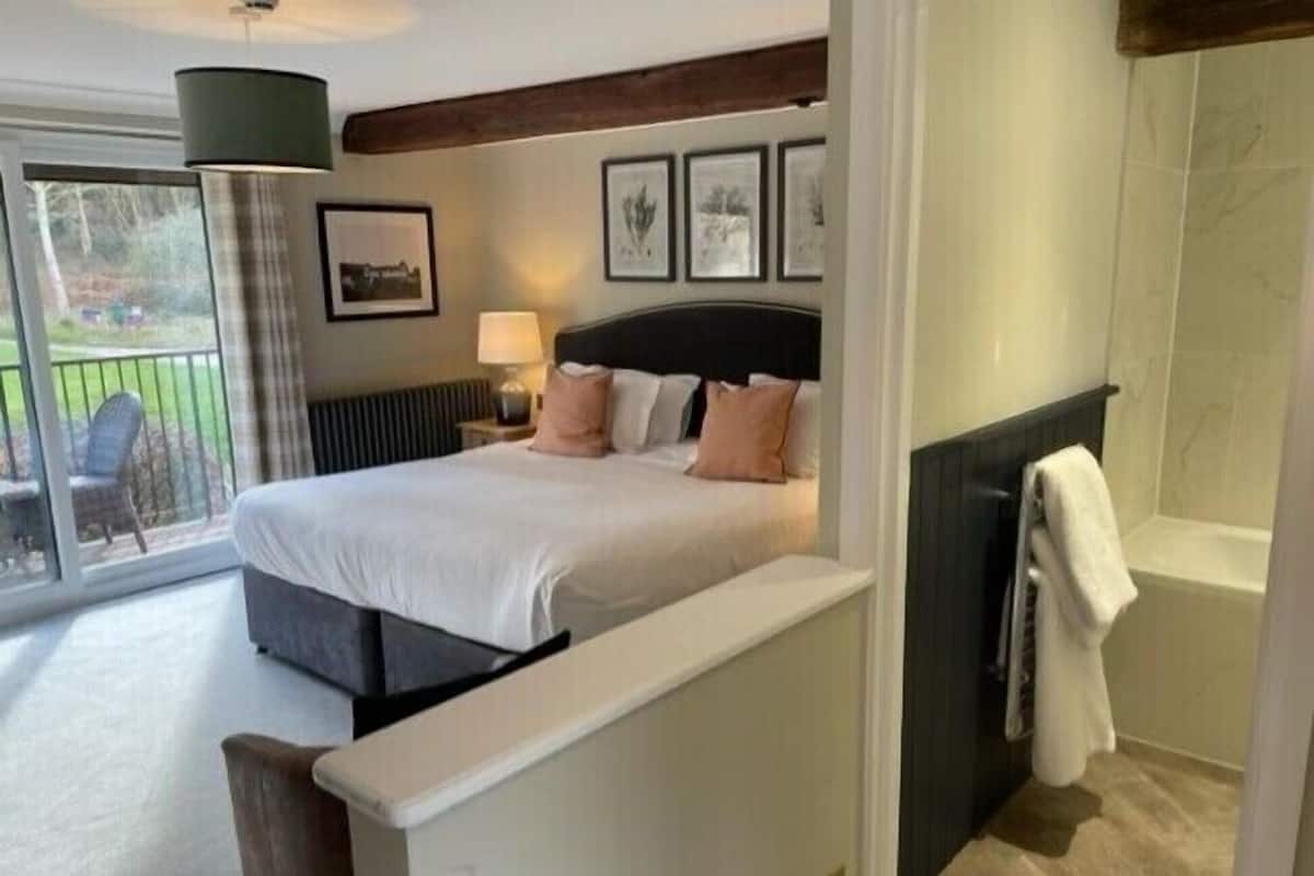 Un dormitorio con cama, mesita de noche, lámpara, ventana con vistas al exterior y zona de ducha.
