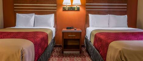 Habitación de hotel con dos camas, una mesita de noche con lámparas y una alfombra estampada.