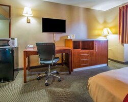 A hotel room with a desk, chair, TV, minibar, and a bed.