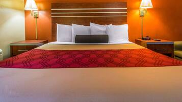 Habitación de hotel con una cama grande, dos mesitas de noche, una lámpara de noche y una colcha de cama roja con estampado, además de dos lámparas fijadas a la pared.