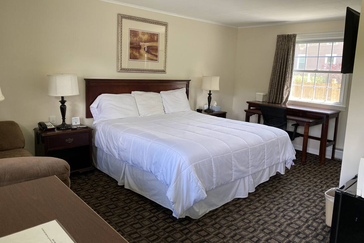 A hotel room with a large bed, two bedside tables with lamps, a desk, and a chair.