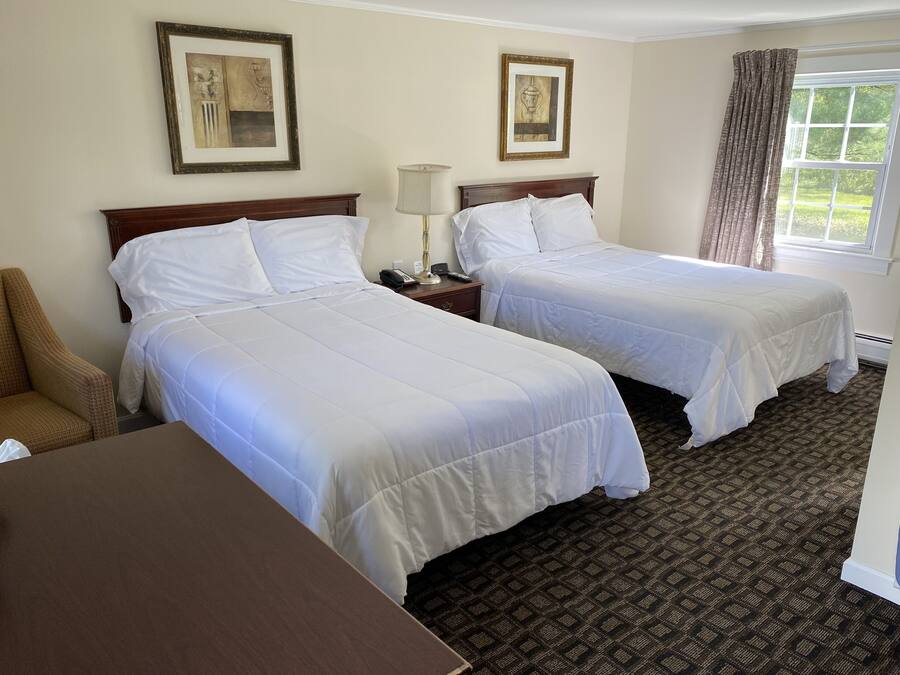 A hotel room with two beds, a chair, a desk, and two framed pictures on the wall.