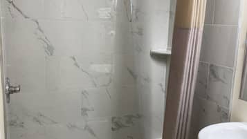 Un baño con ducha de vidrio, bañera blanca y lavamanos con espejo.