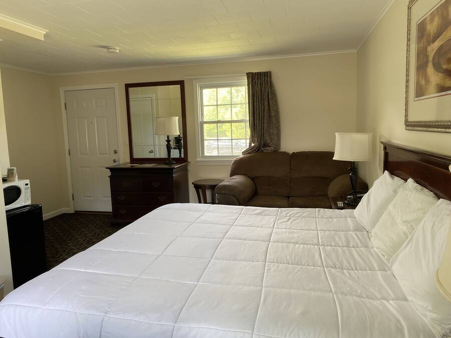 Une chambre d’hôtel avec un grand lit, une commode en bois, un miroir, une fenêtre avec des rideaux et un tableau au mur.