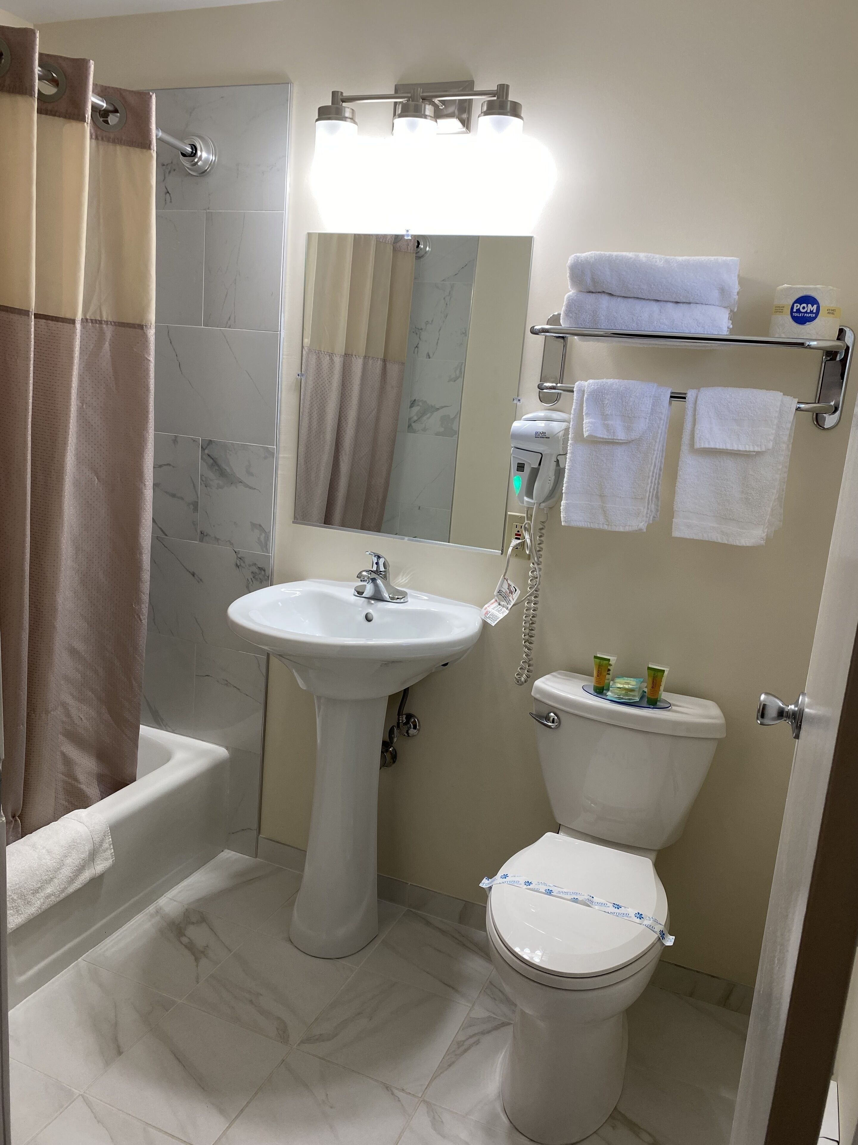 A bathroom with a pedestal sink, a toilet, a shower area, and a towel rack with towels.