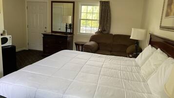 A hotel room with a large bed, a dresser, a chair, a desk with a lamp, and a window with curtains.