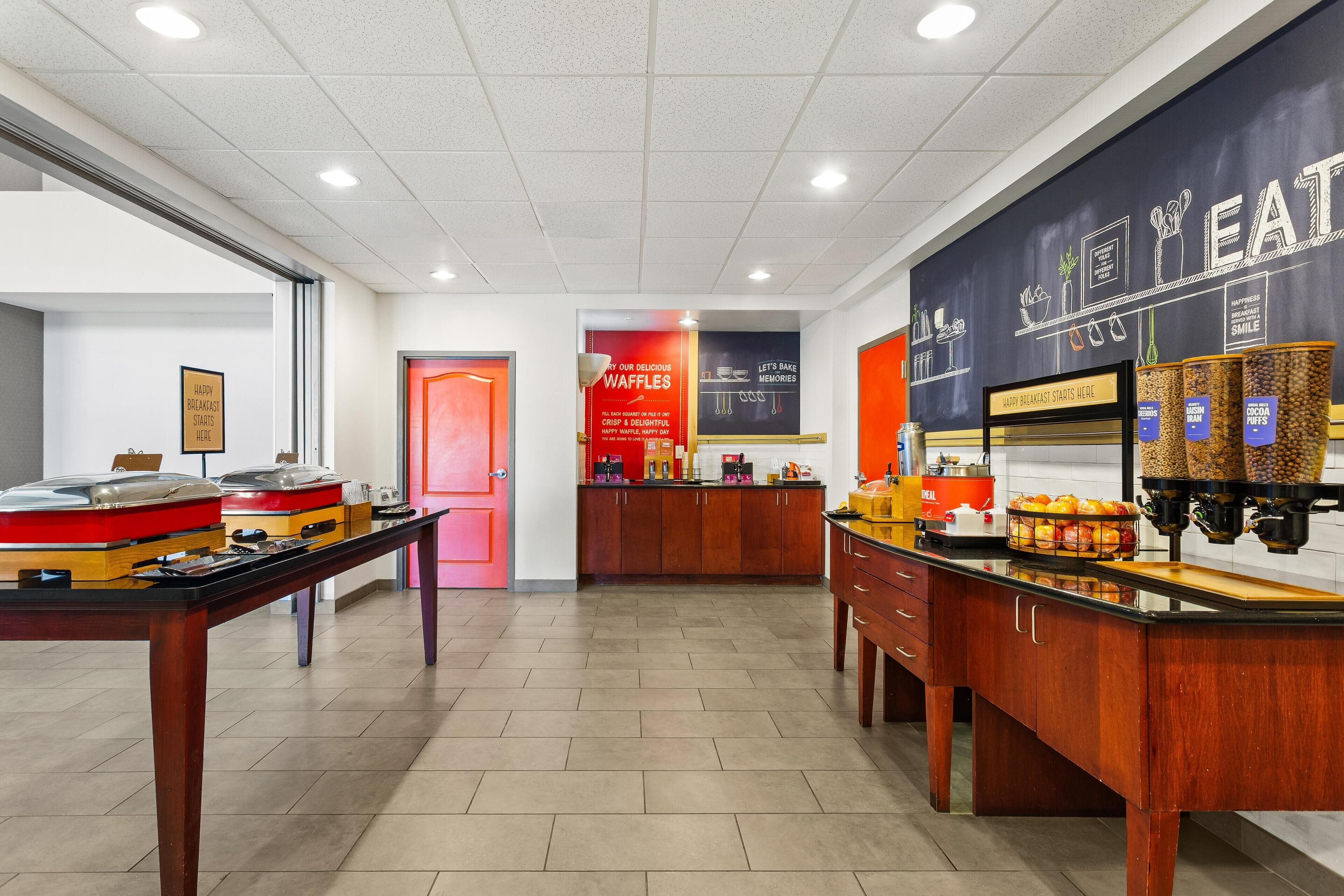 A modern kitchen area with a waffle station, a coffee machine, and a display of various food items.