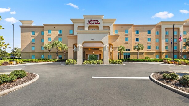 A Hampton Inn & Suites hotel with a central entrance, multiple floors, and a parking lot.