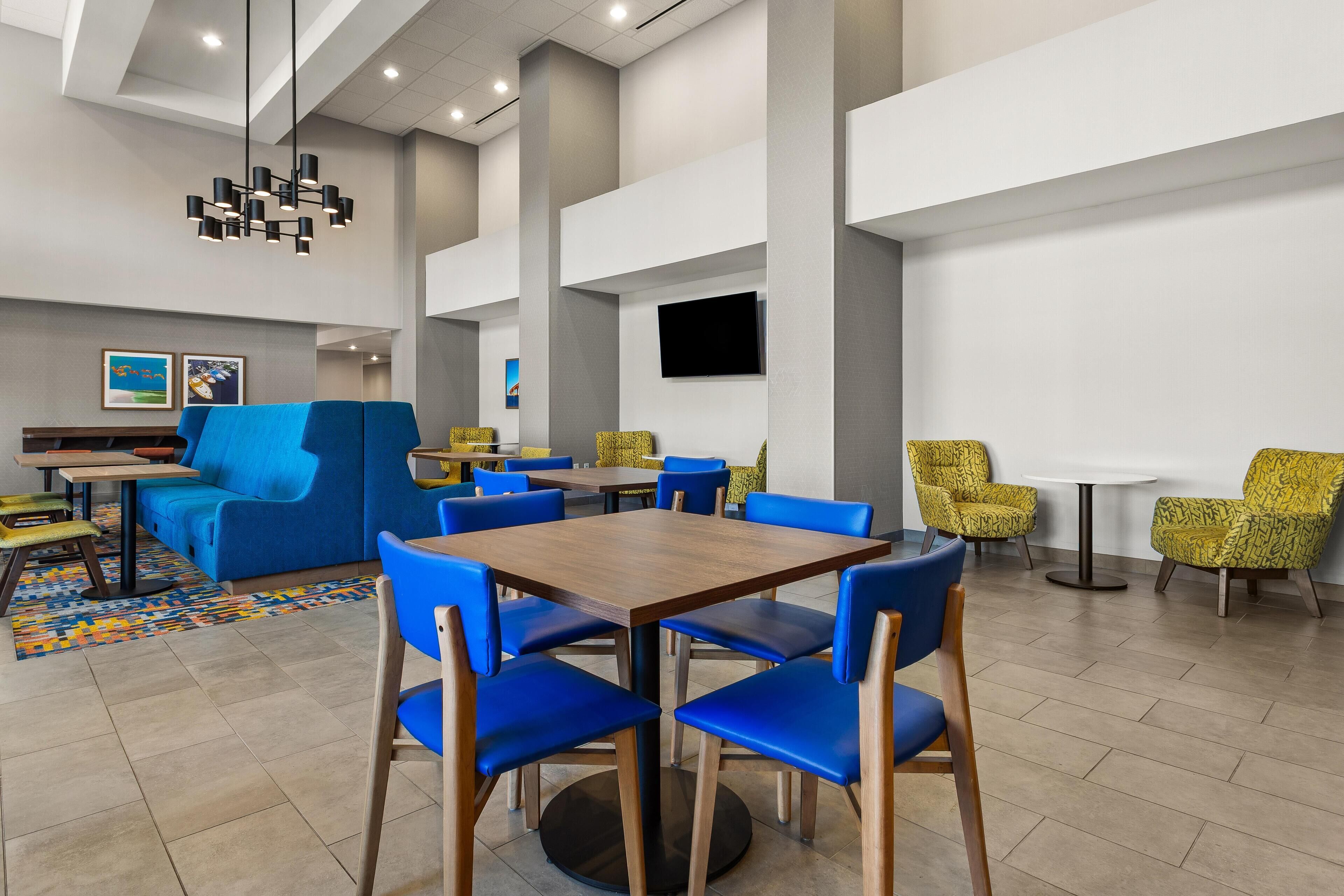 Un comedor moderno con sillas azules y amarillas, una mesa de madera y una alfombra estampada.