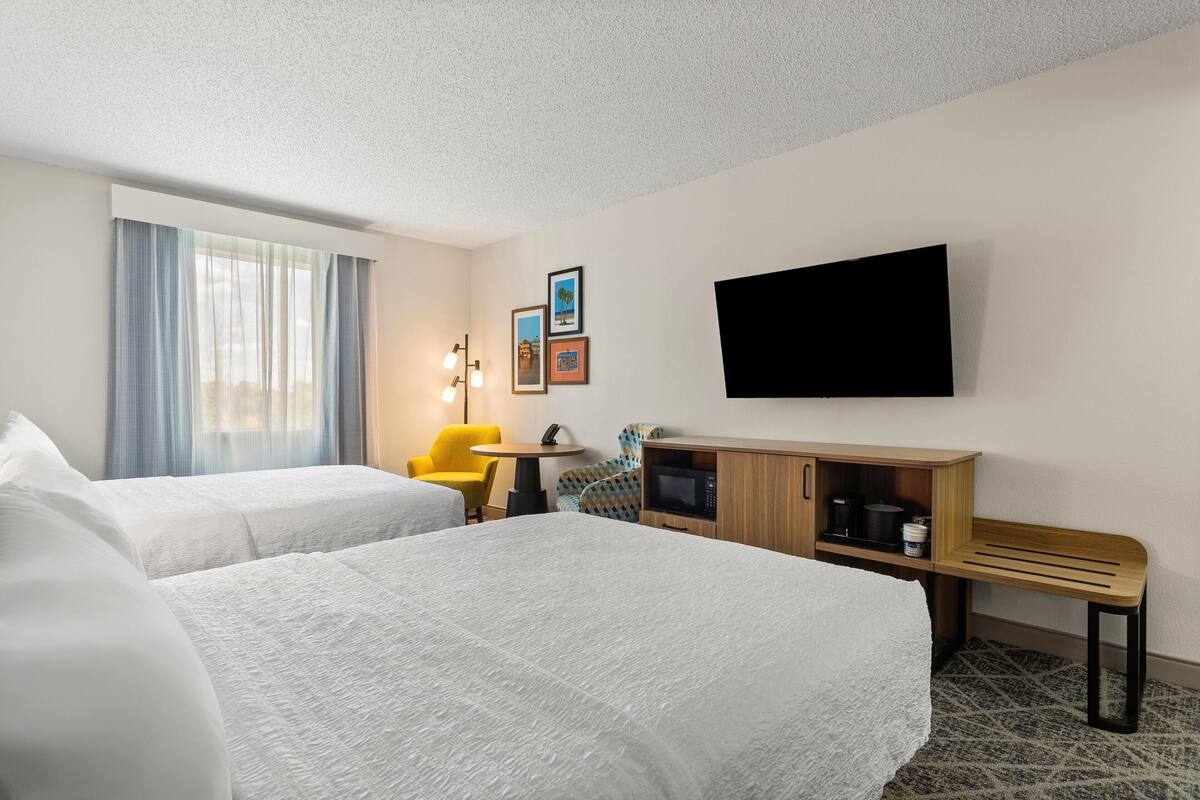 A hotel room with two beds, a desk, a chair, a TV, and a microwave.