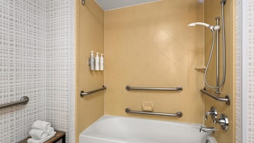 Ein Badezimmer mit Badewanne, Haltegriffen, Duschkopf und Pflegeprodukten auf einem Ablagefach.