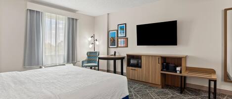 A hotel room with a large bed, a desk, a chair, a TV, and a microwave.