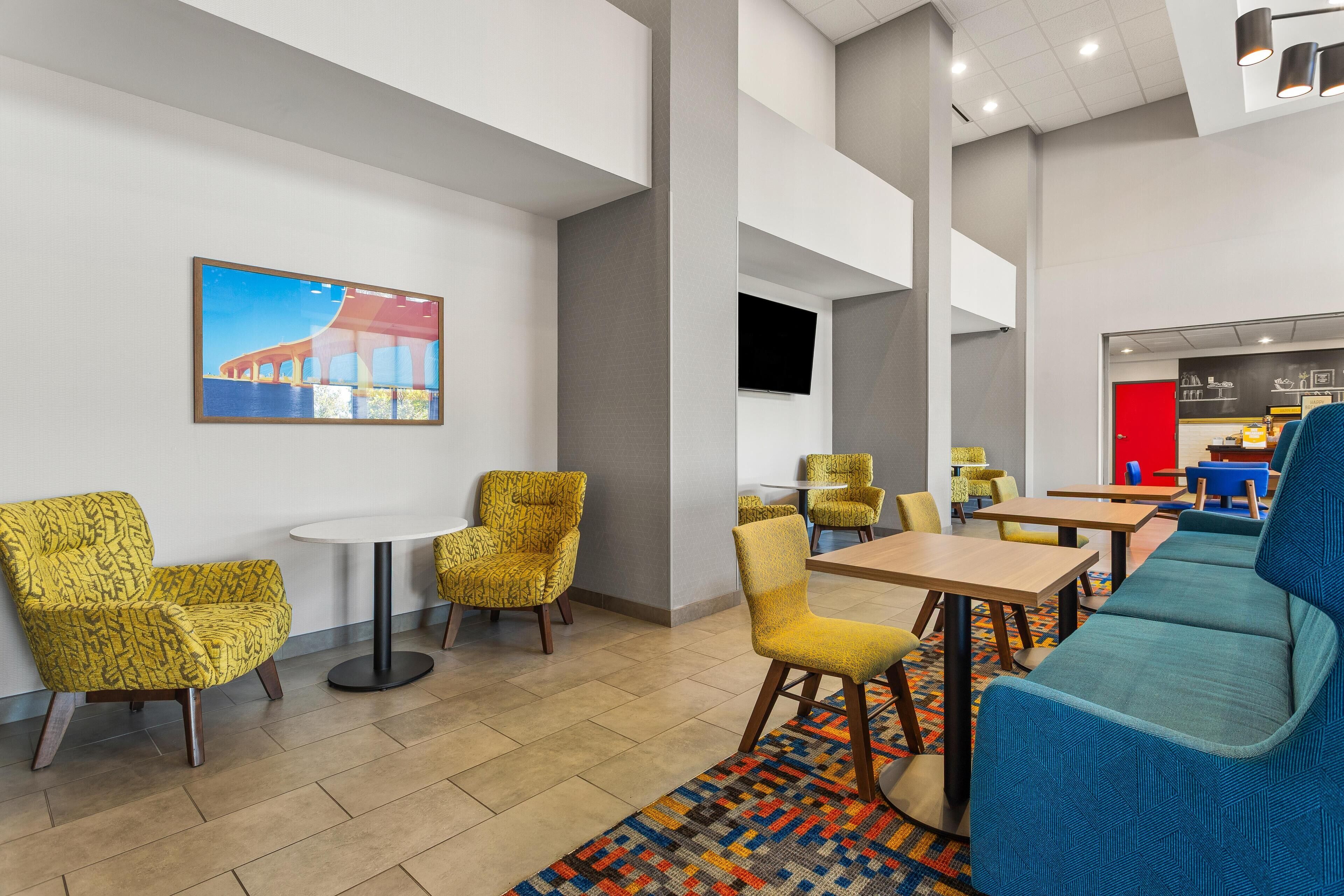 A modern hotel lobby with yellow patterned chairs, a blue sofa, and a colorful rug.