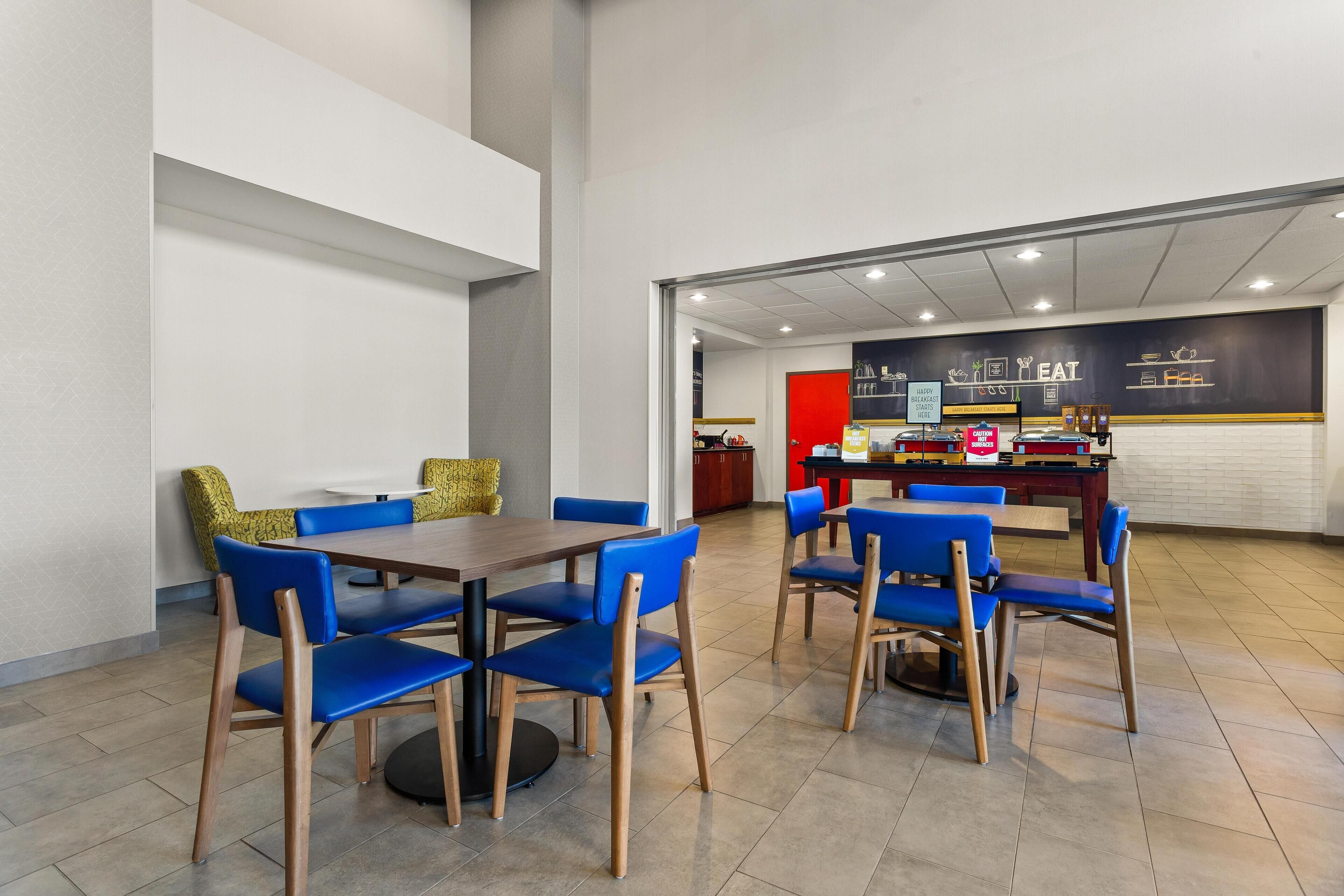 Un comedor moderno con sillas azules y una mesa de madera, una barra con un menú, y una pared roja decorativa.