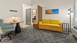 Una sala de estar moderna con un sofá amarillo, un tapete estampado, un sillón azul y amarillo, una mesita redonda y un cuadro en la pared.
