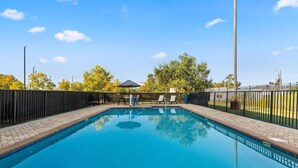 A rectangular swimming pool with a tiled edge, surrounded by a black metal fence.