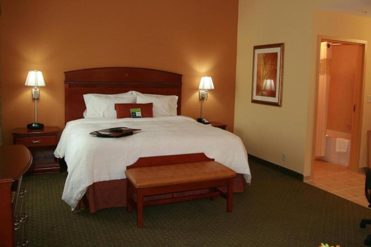 A hotel room with a large bed, bedside tables, a bench, and two lamps.