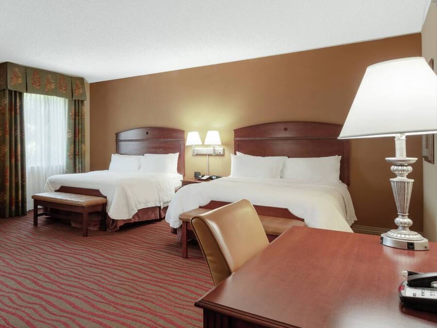 A hotel room with two beds, a desk, and a lamp.