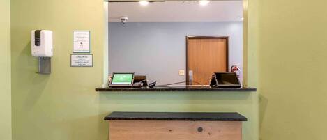 A reception desk with a computer, a check-in/out sign, and a hand sanitizer dispenser.