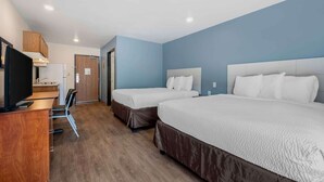 Ein Hotelzimmer mit zwei Betten, einem Schreibtisch, einem Fernseher und einem Kleiderschrank.