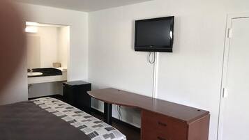 A hotel room with a bed, a desk, a television mounted on the wall, and a small cabinet.