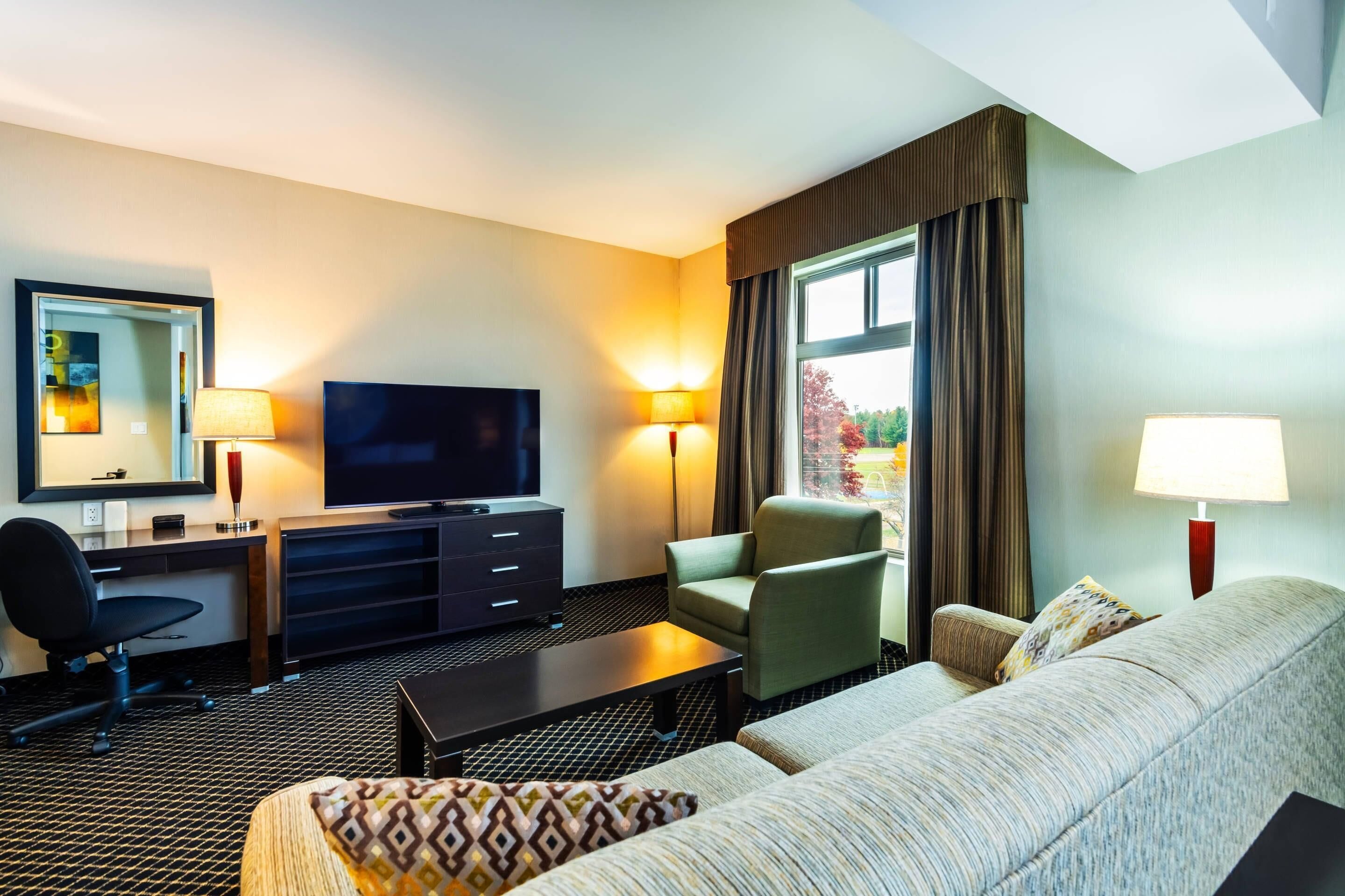 A hotel room with a sofa, armchair, TV, desk, and lamps.