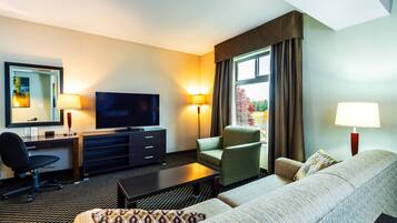 A hotel room with a sofa, armchair, TV, desk, and lamps.