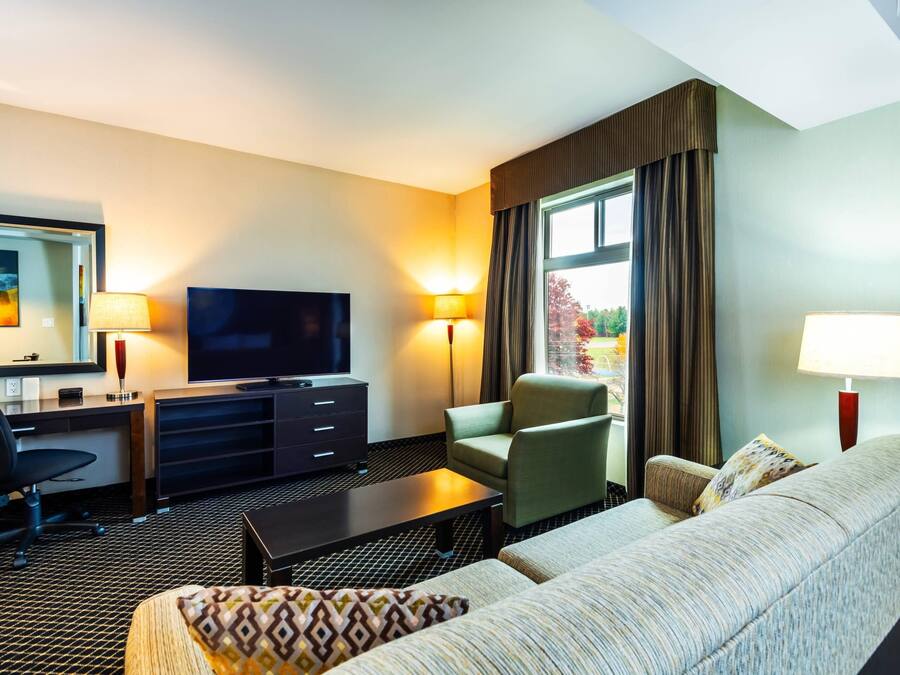 A hotel room with a sofa, armchair, TV, desk, and lamps.