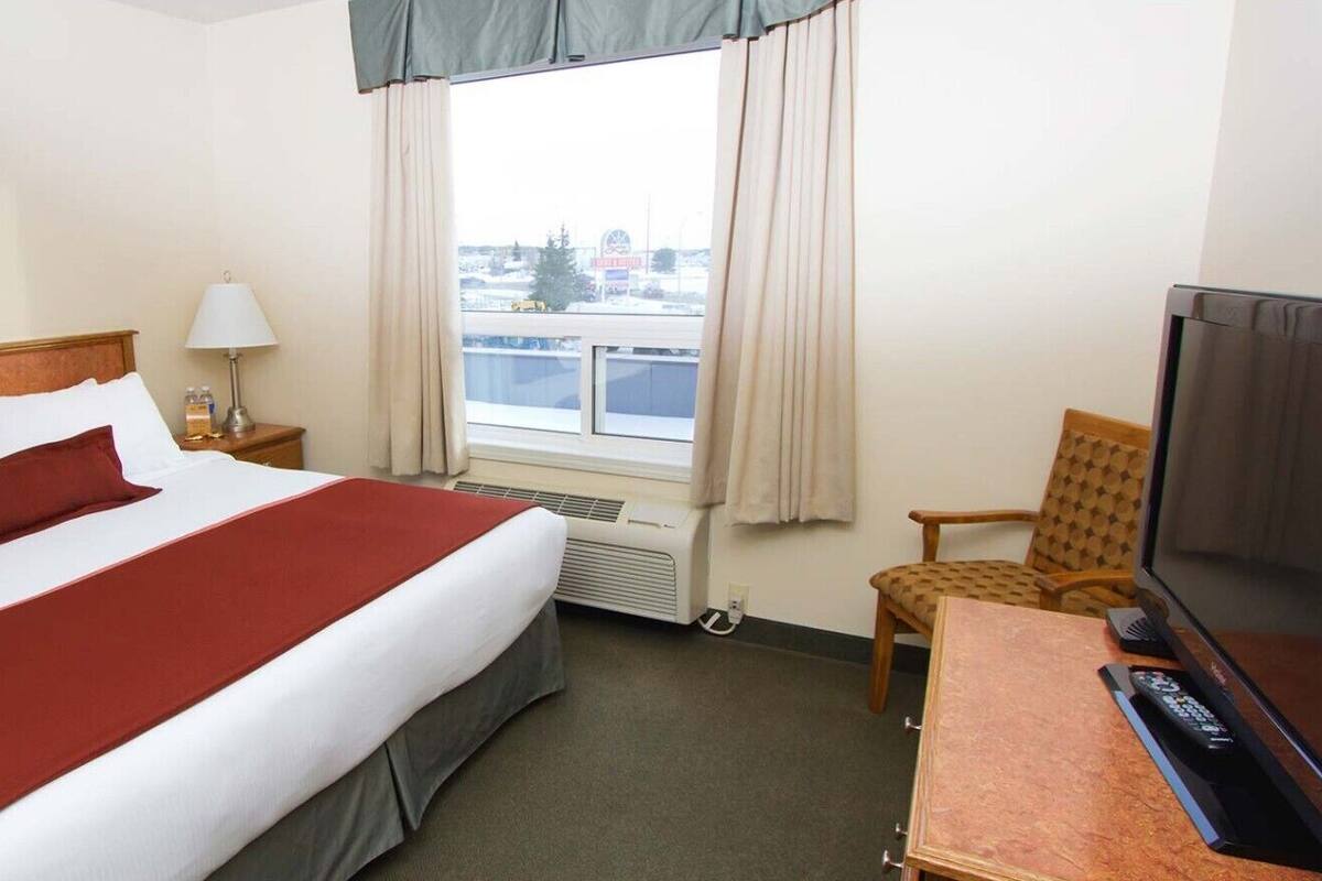 Habitación de hotel con cama, una silla, un televisor y ventana con vistas a edificios.