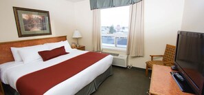 A hotel room with a bed, a chair, a TV, and a window with a view of buildings.
