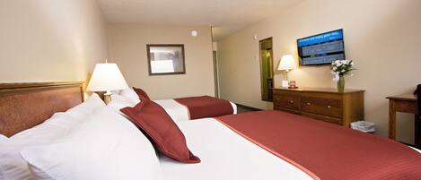 A hotel room with two beds, a wooden headboard, a nightstand with a lamp, a dresser, a mirror, and a television displaying a welcome message.