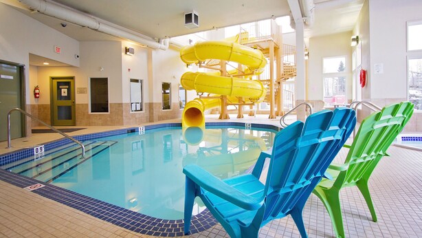 Una piscina interior con tobogán, sillas azules y verdes, y una puerta de salida visible.