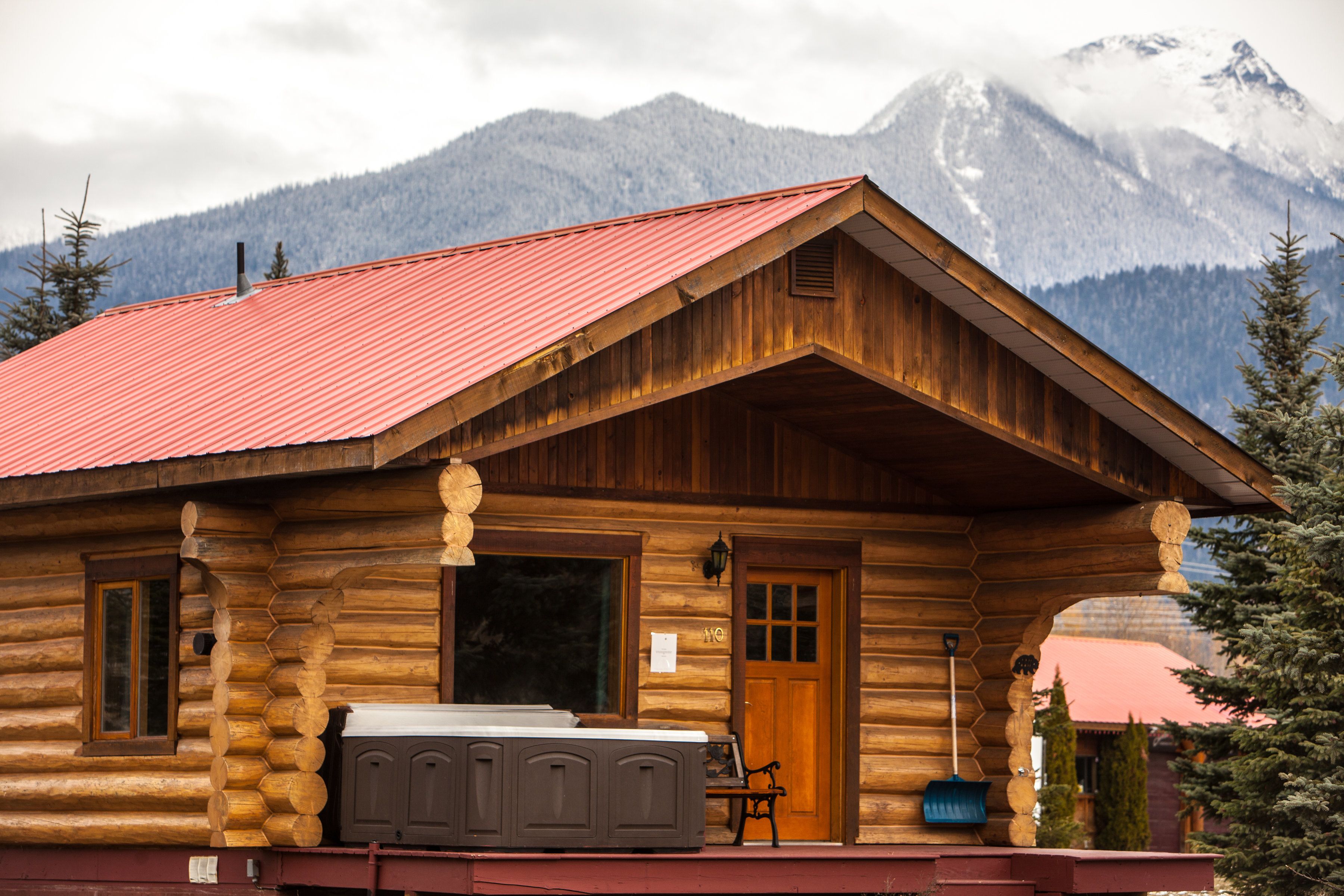 Una cabaña de madera con techo rojo, fachada de madera y un ventanal grande.