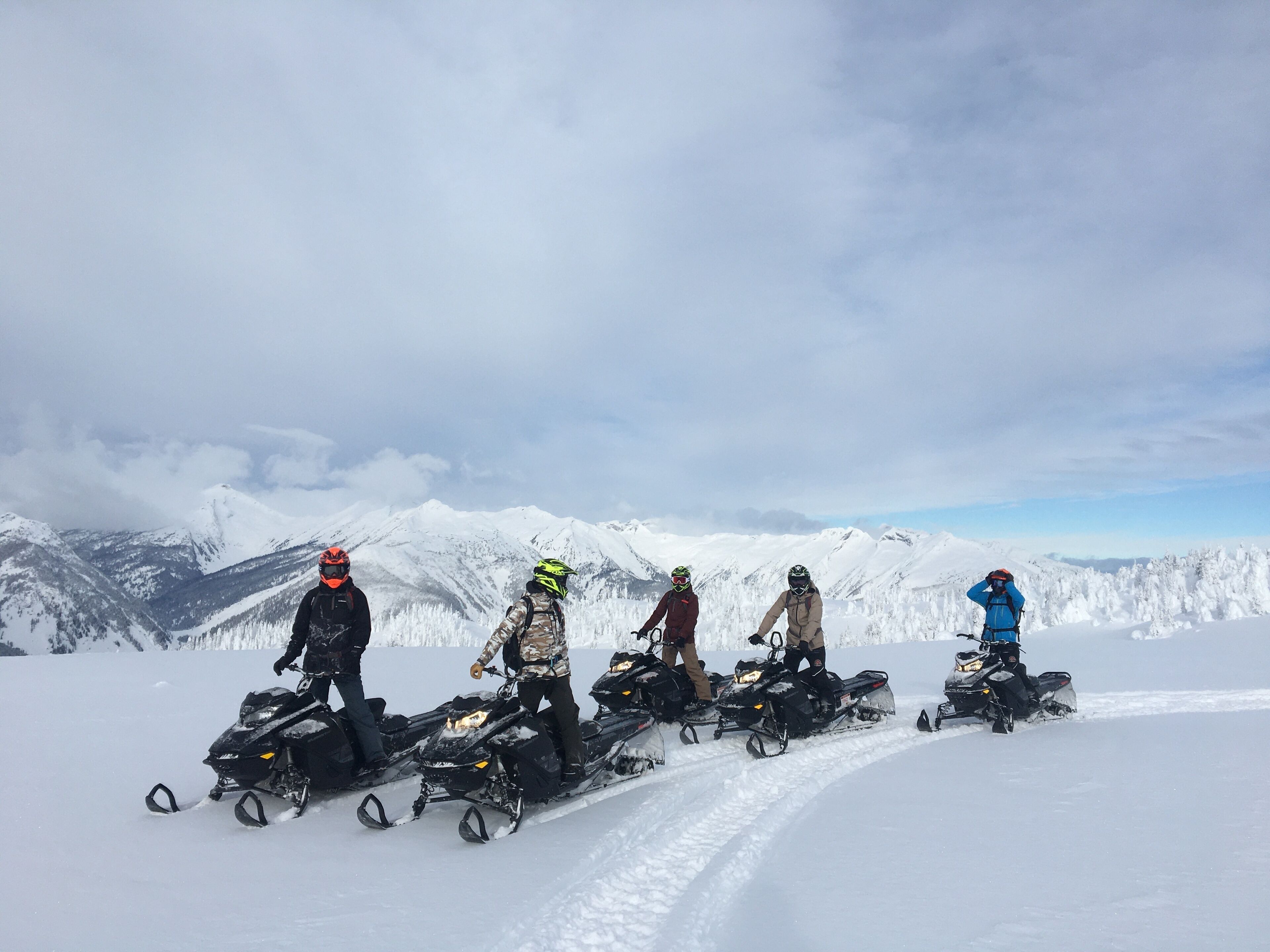 Un grupo de personas en motos de nieve en una montaña nevada con cielo despejado.
