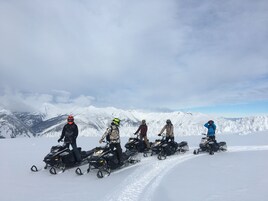 Un grupo de personas en motos de nieve en una montaña nevada con cielo despejado.