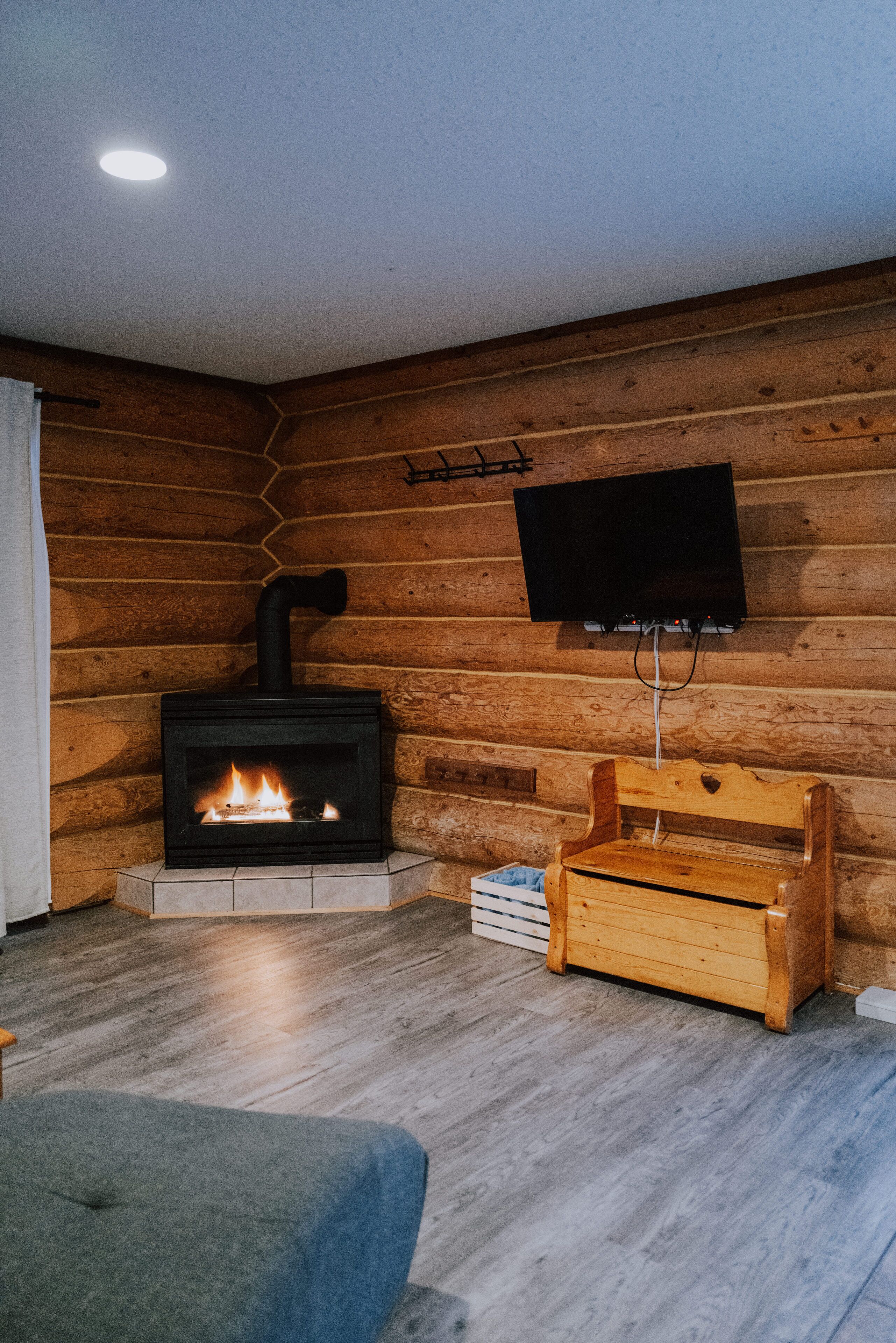 Ein gemütliches Zimmer mit Kaminofen, Wandfernseher und einer hölzernen Sitzbank.