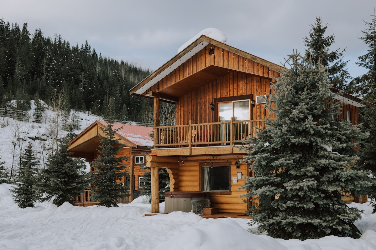 Una cabaña de madera con balcón, rodeada de nieve y árboles.